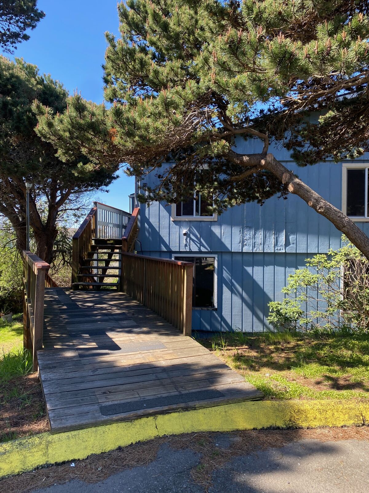 Blue apartment building with a wooden walkway and pine trees on a sunny day at the Coastal Apartments & Storage property